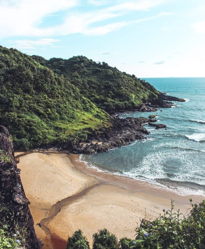 Scenic view of Apsarakonda Beach with lush green hills and clear blue sea near Honnavar, Karnataka.