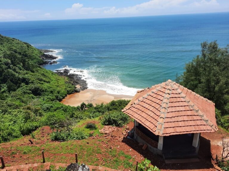 Elevated view of Apsarakonda Beach with red-tiled shelter, green hillside, and waves hitting the golden sand and rocky shore